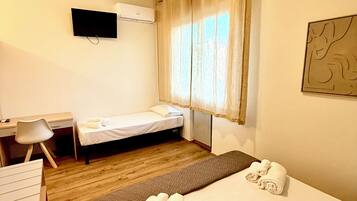 A hotel room with a bed, a desk, a chair, a TV, and a window with curtains.