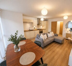 A modern apartment with a dining area, a grey sofa, and a kitchen in the background. - Stylish 2-Bed 2-Bath Apartment with Parking, Lift & Balcony - London & Airports (Croydon)