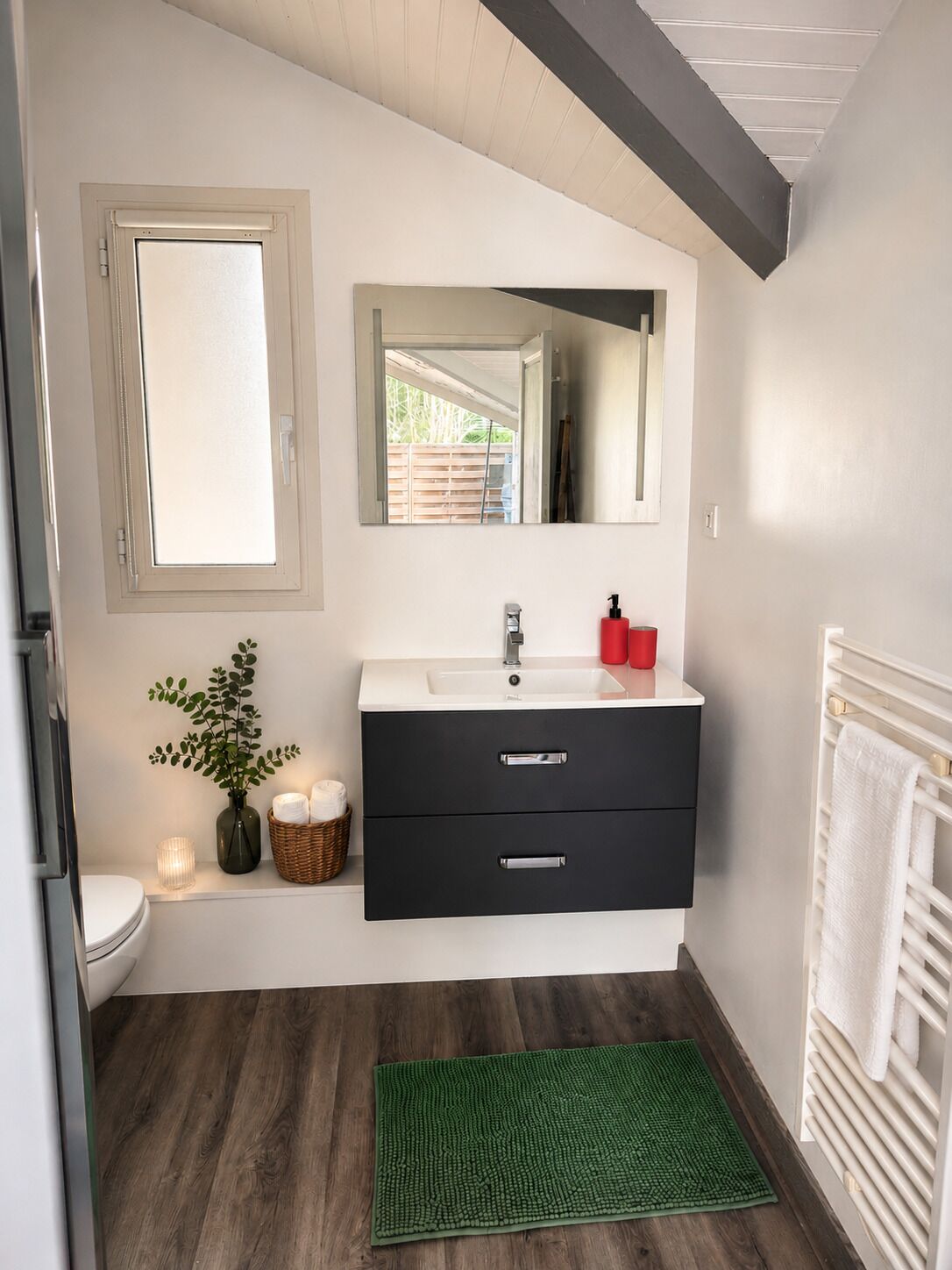 Une salle de bain avec un lavabo blanc, un meuble-lavabo noir, un miroir, un tapis de bain vert et un porte-serviettes blanc.