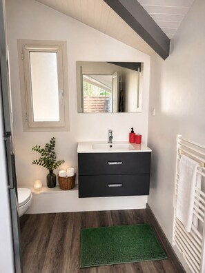 Une salle de bain avec un lavabo blanc, un meuble-lavabo noir, un miroir, un tapis de bain vert et un porte-serviettes blanc.