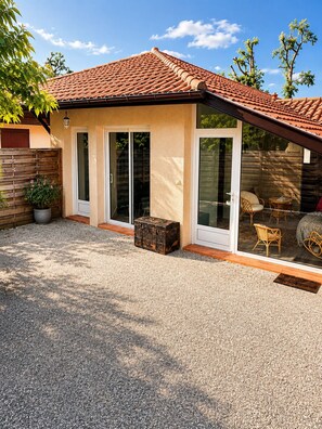 Ein Haus mit einem Ziegeldach, Schiebegläsern, einer Schotterauffahrt und Gartenmöbeln.