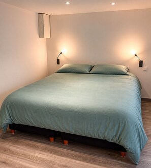 Un lit recouvert d’une couvre-lit verte, deux lampes de chevet et un luminaire fixé au mur.