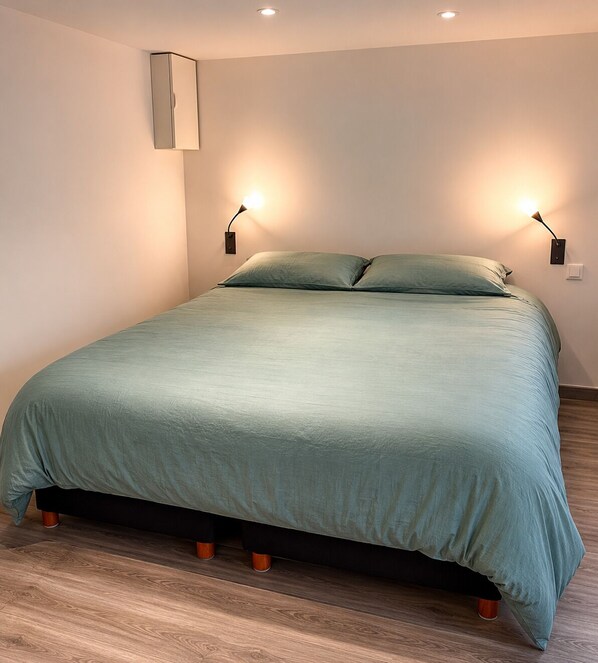 Ein Bett mit grüner Bettdecke, zwei Nachttischlampen und einer Wandleuchte.