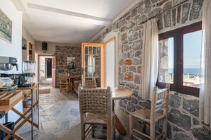 A stone-walled room with a dining area, a view through a window, and a door leading to another room. - Apartment 'Castle Rizaraki 204' with Sea View, Wi-Fi and Air Conditioning (Γύθειο)