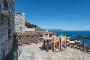 A stone building with a wooden deck, a table, and chairs. - Apartment 'Castle Rizaraki 204' with Sea View, Wi-Fi and Air Conditioning (Γύθειο)
