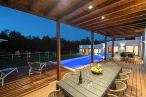 An outdoor deck with a pool, lounge chairs, and a dining table with a bottle and glasses. - Villa Istria Green (Kršan)