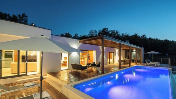 Una casa moderna amb piscina, mobiliari exterior i una zona de porxo coberta.