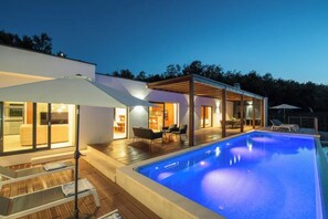 Een modern huis met een zwembad, buitenmeubels en een overdekt terras.