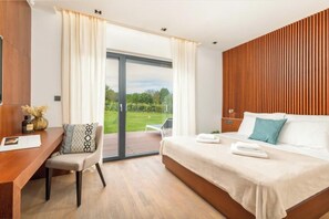 Een moderne hotelkamer met een groot bed, een bureau en uitzicht op een tuin door een schuifdeur.