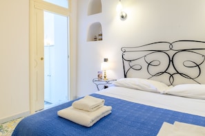Ein Hotelzimmer mit Bett, Nachttisch, Lampe und einer Tür, die auf einen Balkon führt.