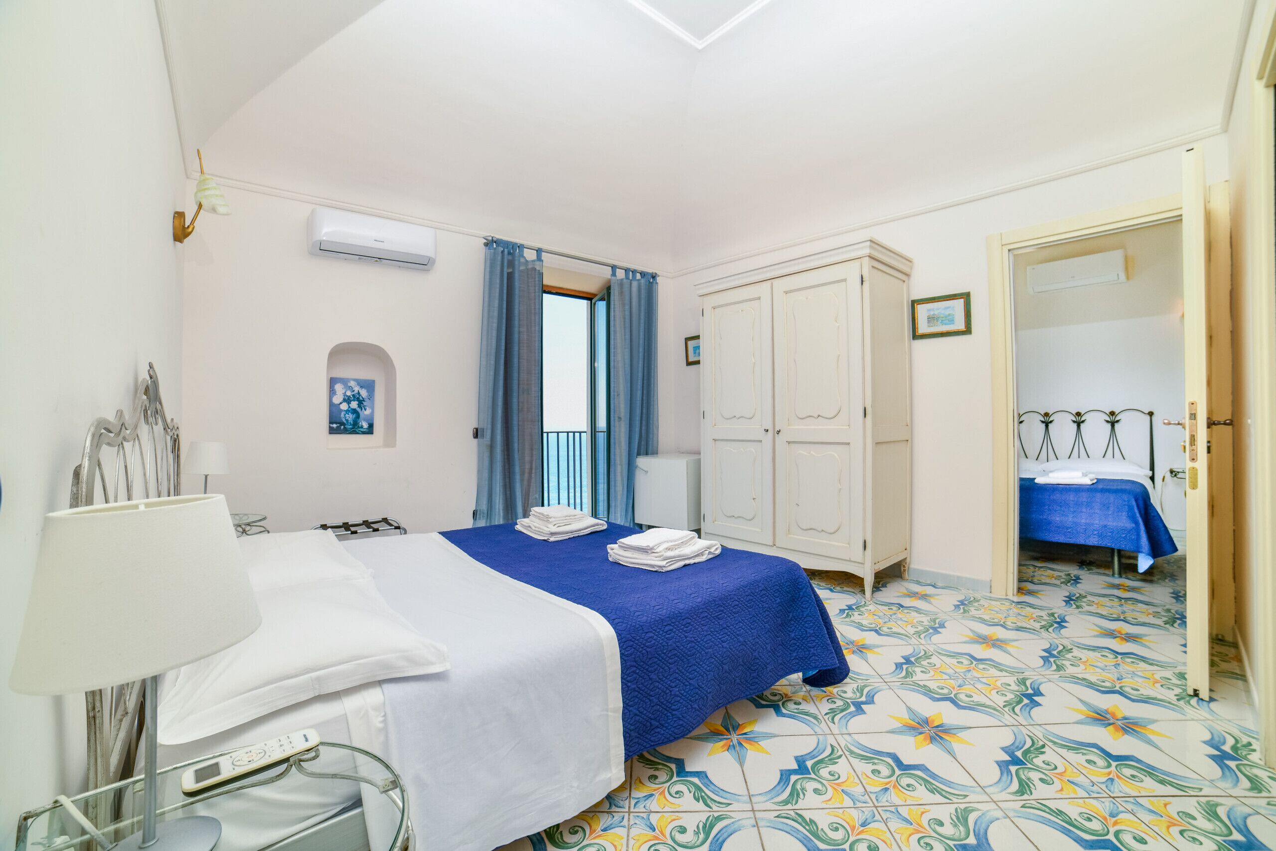 Una habitación de hotel con cama, mesita de noche, lámpara, armario y baño con ducha.