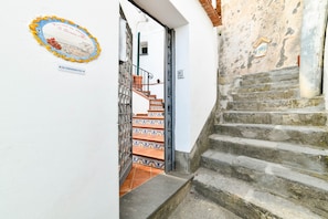 Eine Treppe führt zu einem Raum mit Fliesenboden und einer Tür, deren Eingang mit einem Metallgitter versehen ist.