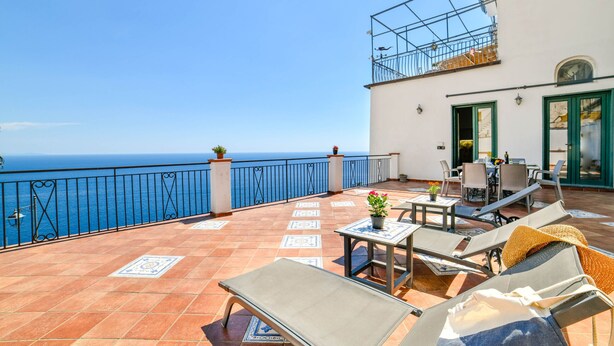 Eine Terrasse mit Liegestühlen, einem Tisch und Stühlen sowie Blick auf das Meer.