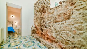 Ein Zimmer mit einer Steinwand, einem Bett mit blauer Bettdecke und einem gefliesten Boden mit Blumenmuster.