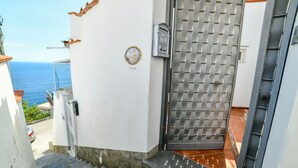 Ein weißes Gebäude mit einem Metallgitter, einer Treppe, die zu einer Terrasse führt, und Blick auf das Meer.