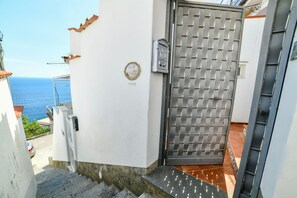 Ein weißes Gebäude mit einem Metallgitter, einer Treppe, die zu einer Terrasse führt, und Blick auf das Meer.