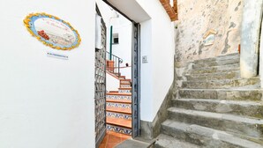 Eine Treppe führt zu einem Raum mit Fliesenboden und einer Tür, deren Eingang mit einem Metallgitter versehen ist.