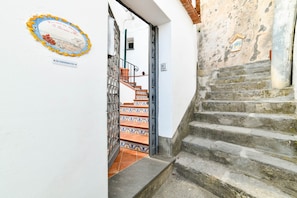 Eine Treppe führt zu einem Raum mit Fliesenboden und einer Tür, deren Eingang mit einem Metallgitter versehen ist.