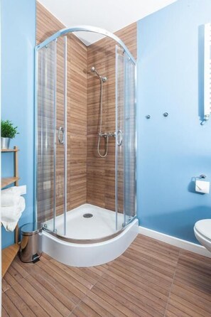 A shower enclosure with a glass door, a wooden floor, and a blue wall.