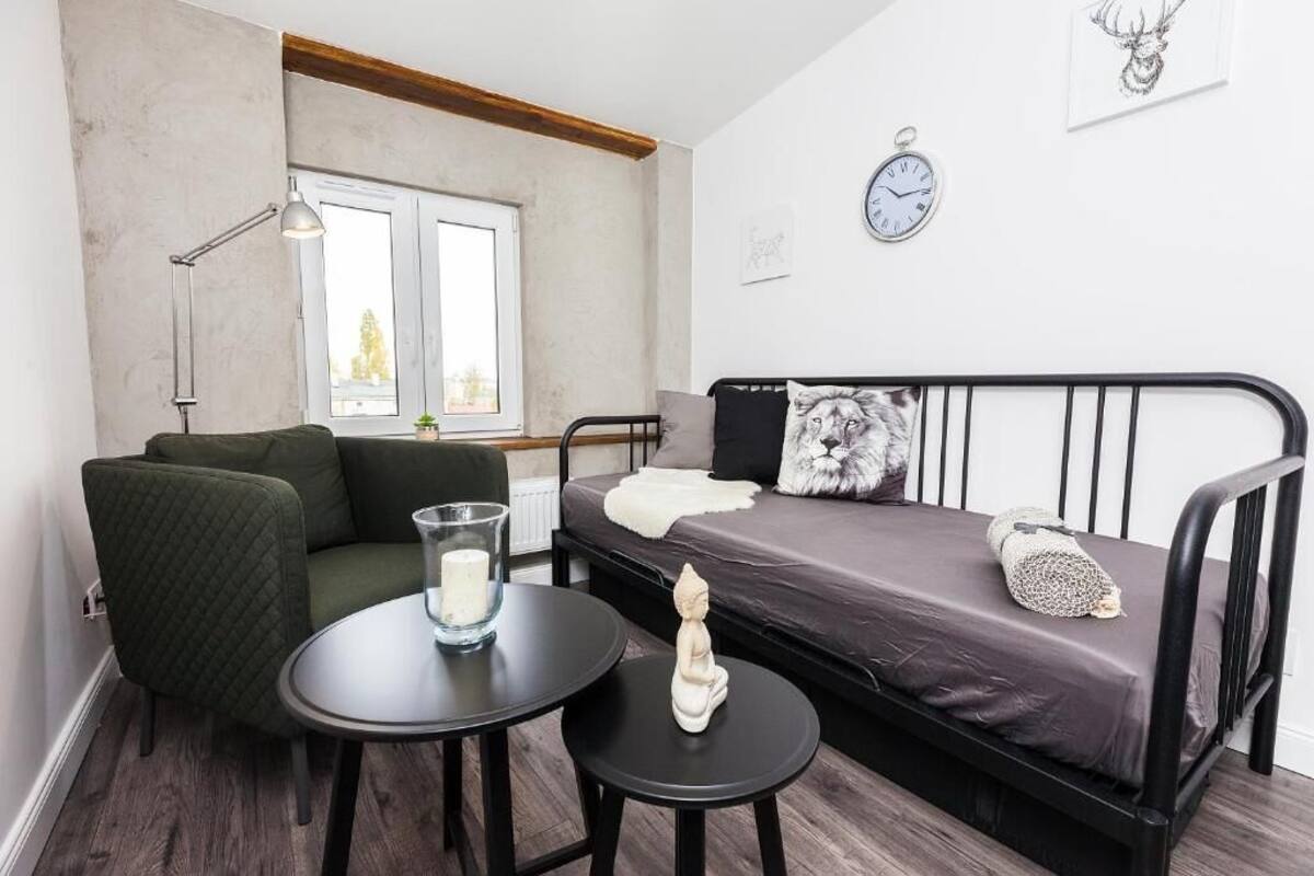A small, modern room with a bed, a green armchair, a round table with a candle, and a window.