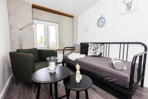 A small, modern room with a bed, a green armchair, a round table with a candle, and a window. - Book-Apart Fabryczna (Łódź)