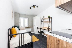 Una habitación compacta con cama, escritorio, silla y kitchenette.