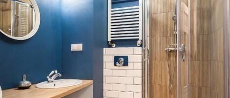 A bathroom with a shower, toilet, and sink, featuring blue walls and wooden flooring.