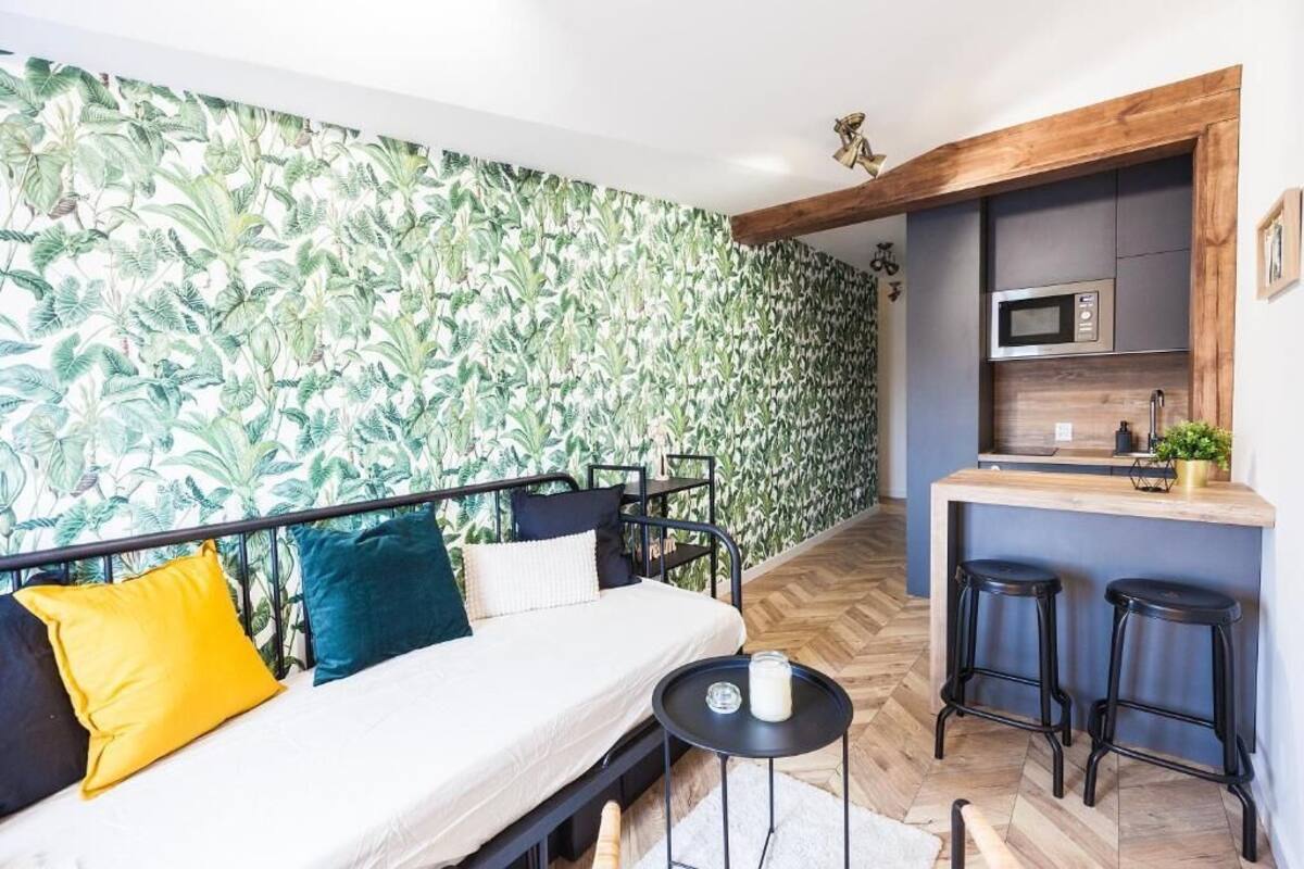 A compact living space with a sofa, a small round table, a kitchenette, and a herringbone-patterned floor.