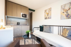 A compact living space with a kitchenette, a sofa, and artwork on the walls. - Book-Apart Fabryczna (Łódź)