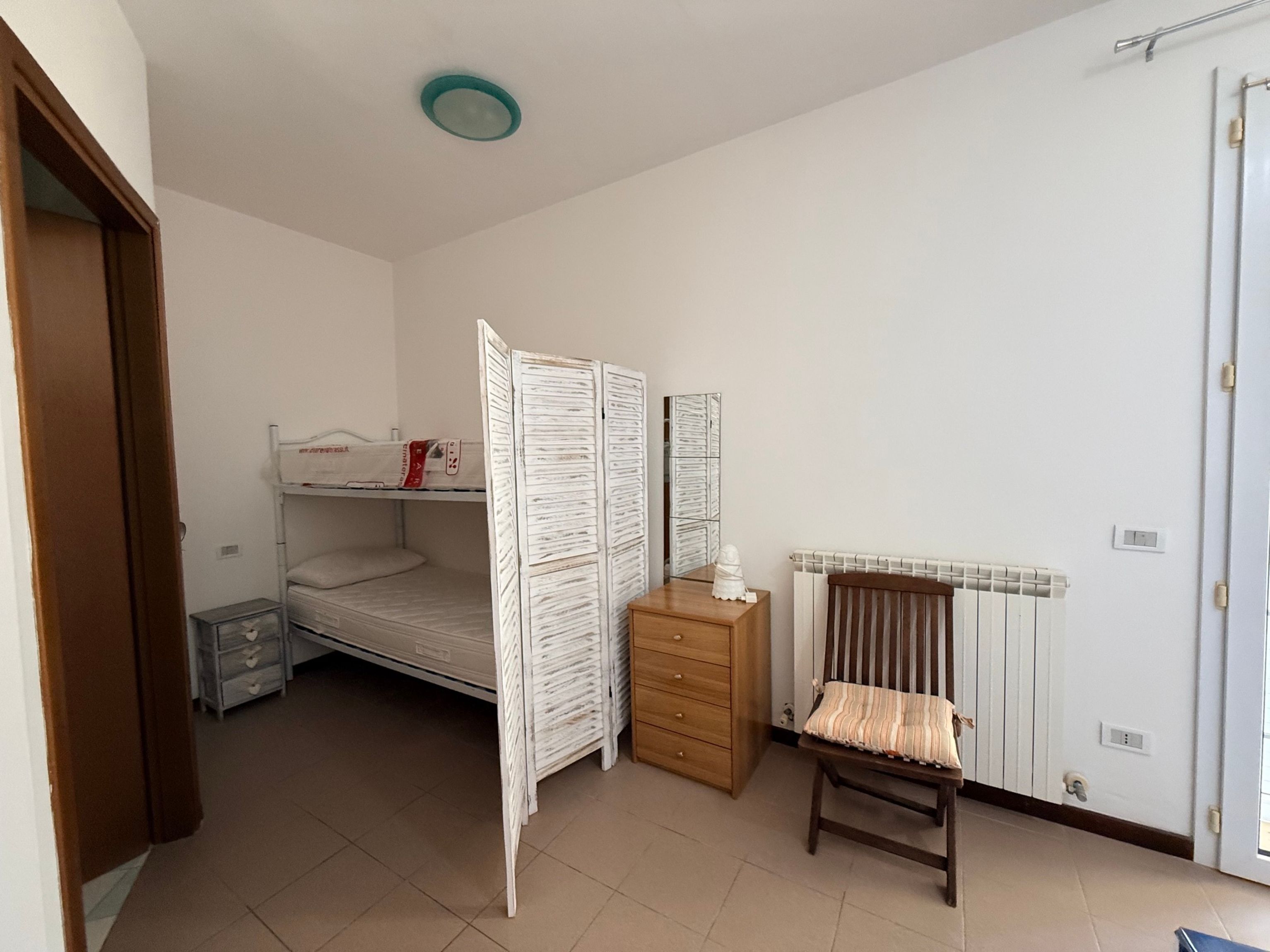 Une chambre avec un lit superposé, une commode en bois, une chaise et un radiateur.