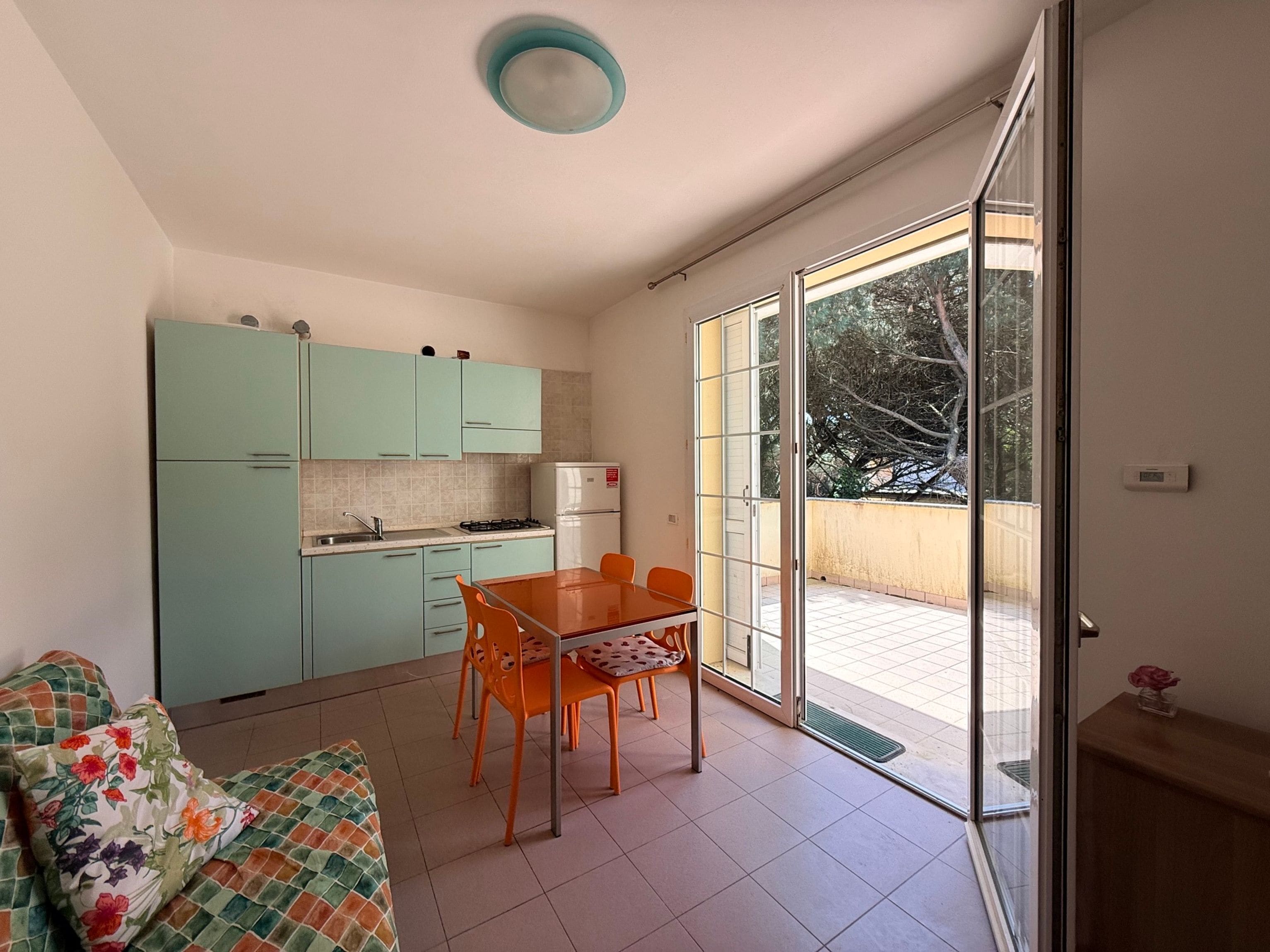 Uma cozinha compacta com mesa e cadeiras, um sofá e uma porta de vidro deslizante para uma varanda.