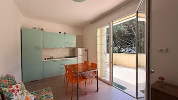 Uma cozinha compacta com mesa e cadeiras, um sofá e uma porta de vidro deslizante para uma varanda.