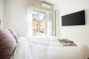 Ein Schlafzimmer mit Bett, einem fensterbelaubten Fenster, einer Klimaanlage und einem flachbildfernseher an der Wand.