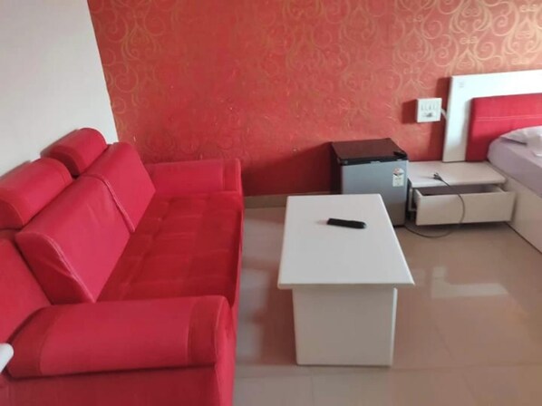Un sofá rojo, una mesa blanca y un mueble gris pequeño en una habitación con papel tapiz estampado.