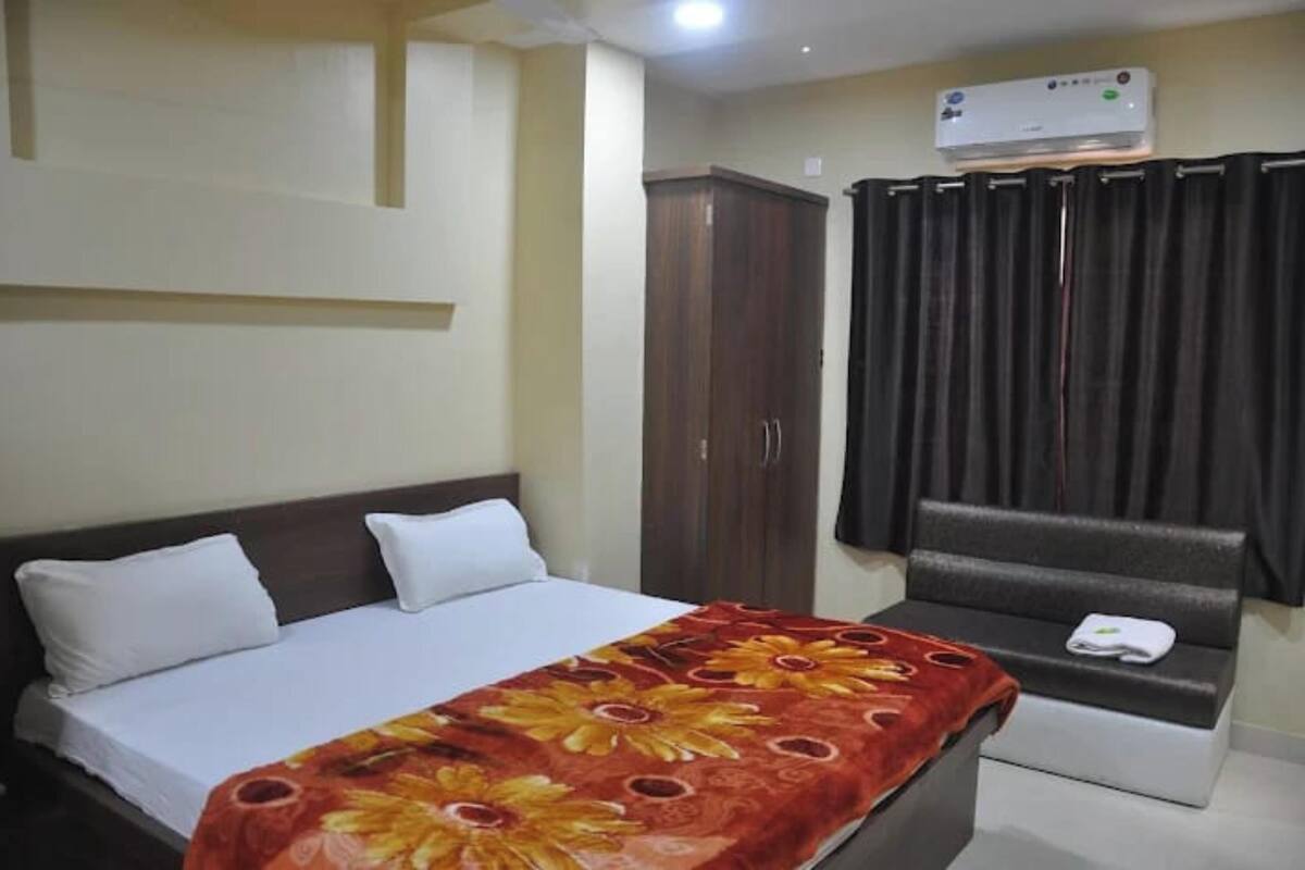 A hotel room with a bed, a sofa, a wardrobe, and an air conditioning unit.