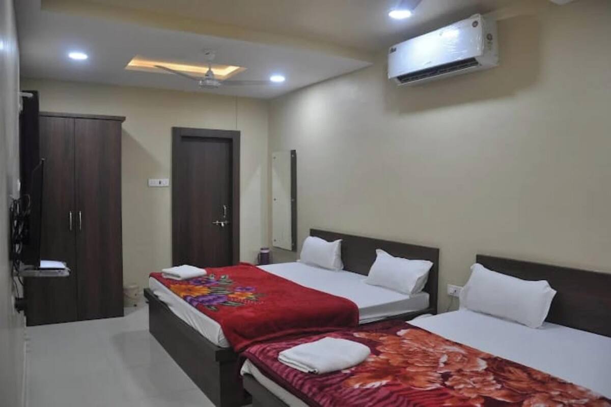 A hotel room with two beds, a wardrobe, an air conditioning unit, and a ceiling fan.