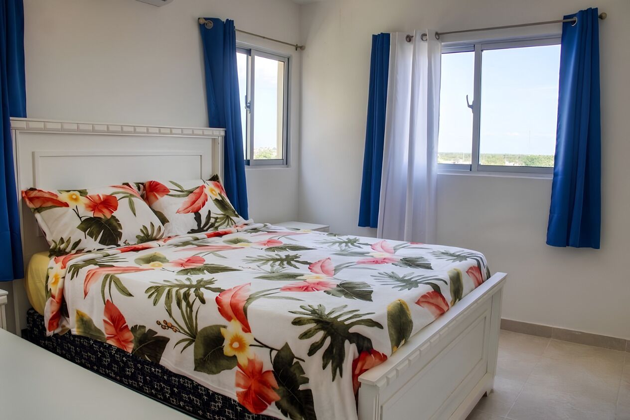 Une chambre à coucher avec un lit, deux fenêtres et des rideaux bleus.