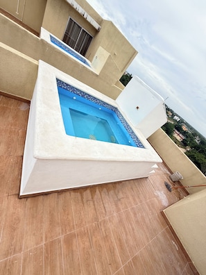 Ein Dachpool mit gefliestem Rand, umgeben von einem beige gefärbten Gebäude mit Fenster und Tür.