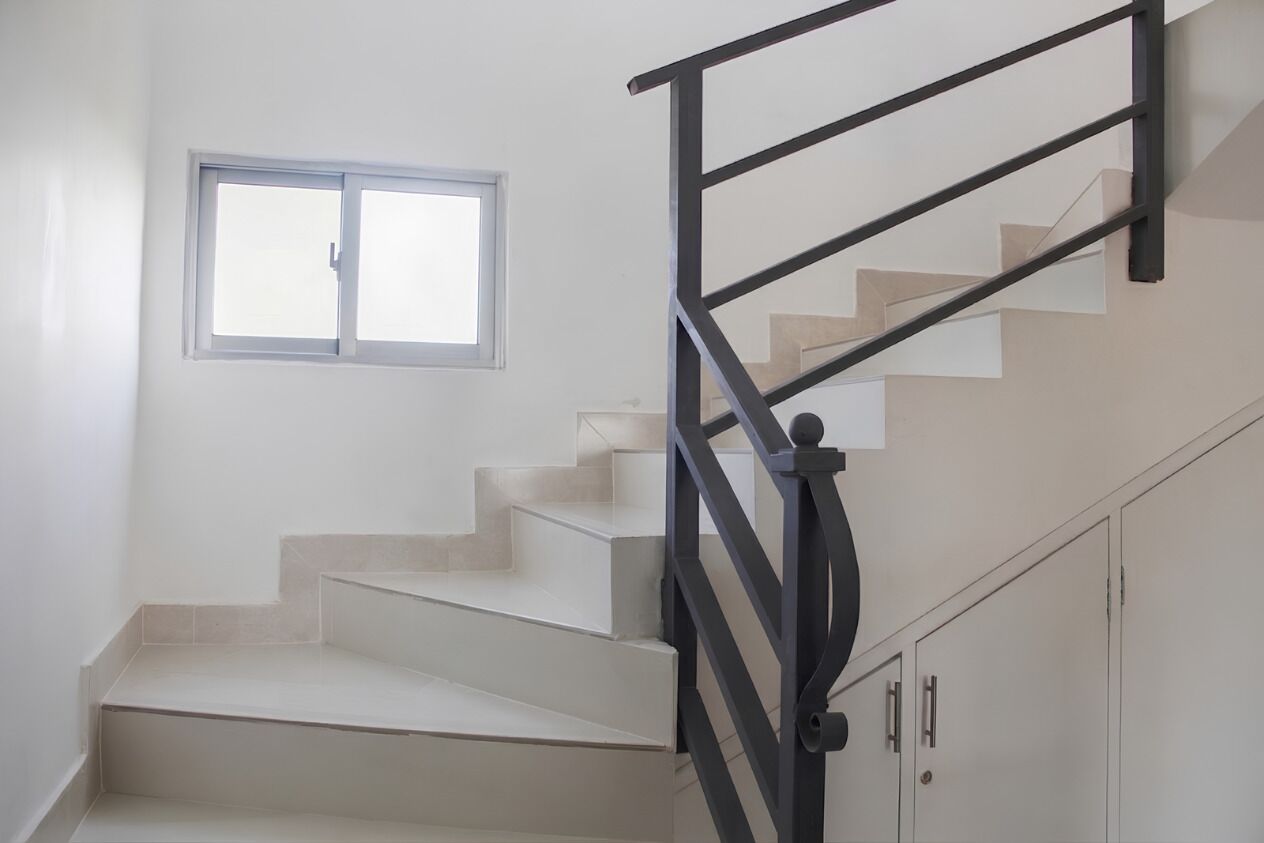 A staircase with a black metal railing, a window, and a set of beige cabinets.