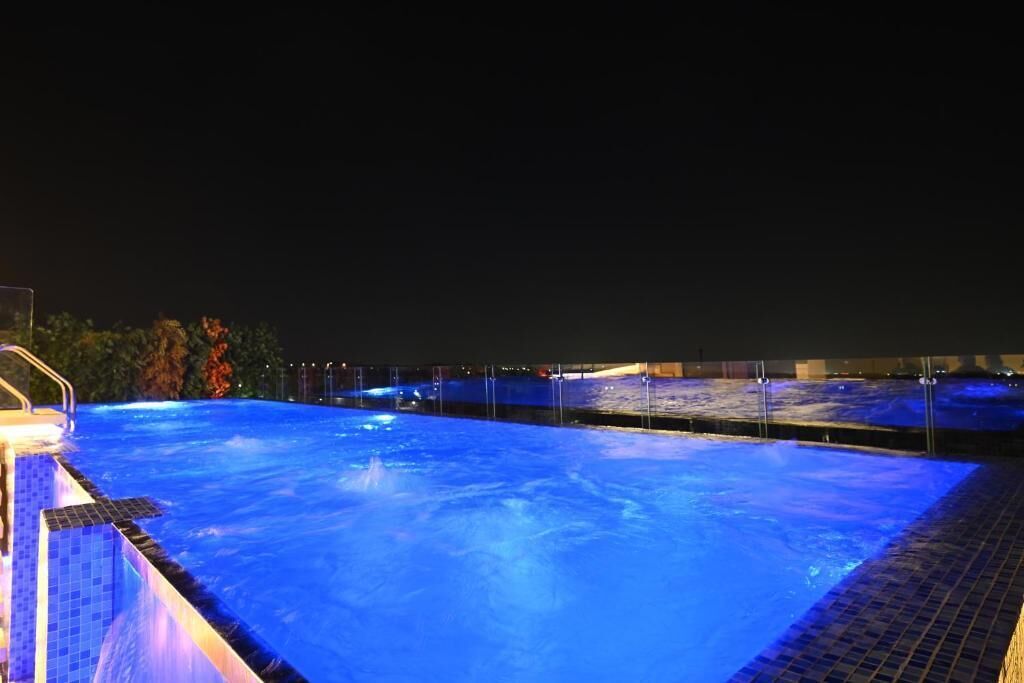 Une piscine éclairée la nuit, avec un bord carrelé et un garde-corps en métal.