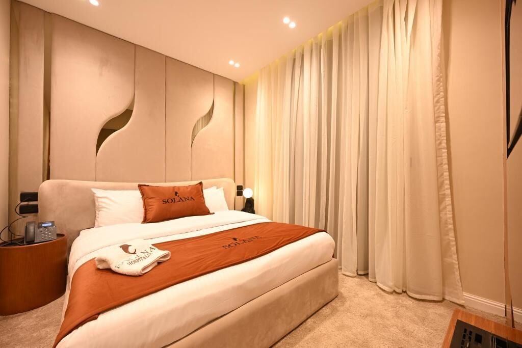 Una habitación de hotel con una cama grande, una mesita de noche con un teléfono y una cortina.
