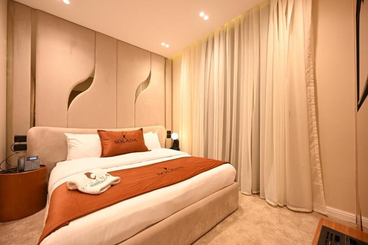 Ein Hotelzimmer mit einem großen Bett, einem Nachttisch mit Telefon und einem Vorhang.