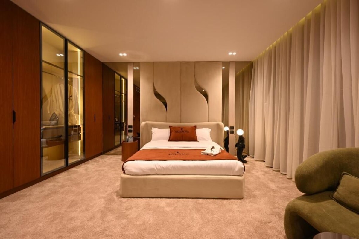 Ein Schlafzimmer mit einem großen Bett, einem Nachttisch, einem Sessel, einem Kleiderschrank und einem Spiegel.