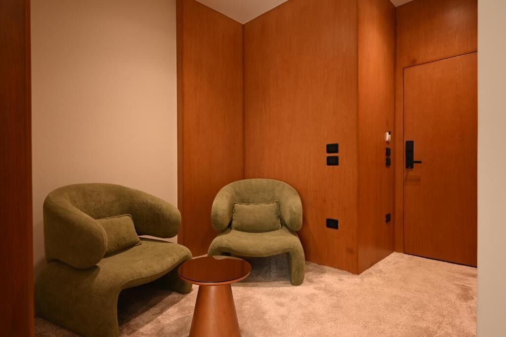 Una habitación con dos sillones verdes, una mesa redonda pequeña y un armario de madera.