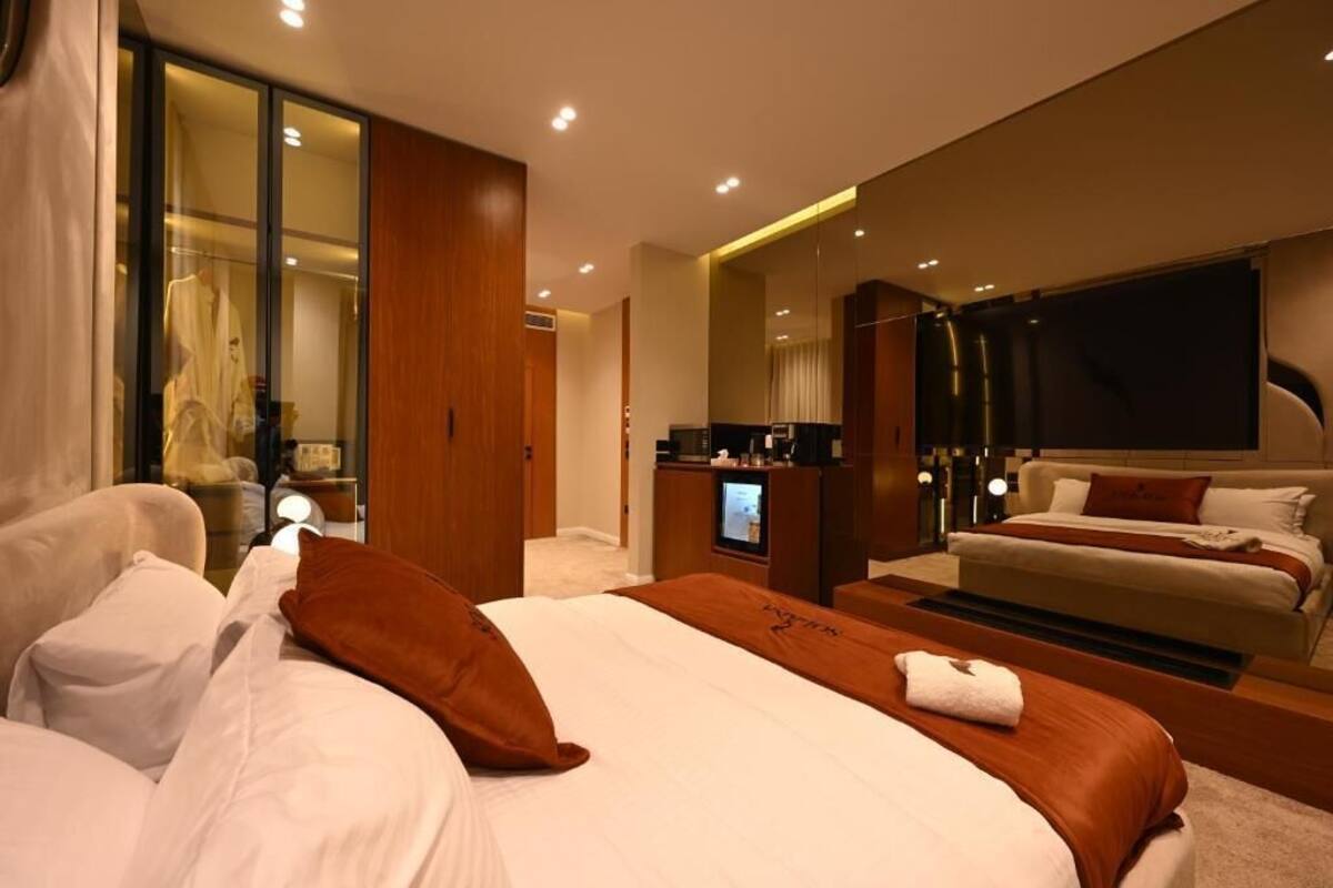 A modern hotel room with a large bed, a desk with a computer, a mirror, and a television.