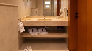 Ein schmales Badezimmer mit Toilette, Waschbecken und Spiegel. Auf dem Boden liegen Hausschuhe und ein Handtuch hängt an der Wand.