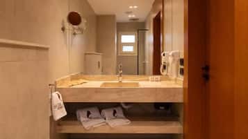 A narrow bathroom with a toilet, sink, and mirror. There are slippers on the floor and a towel hanging on the wall.