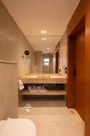 Un baño pequeño con inodoro, lavamanos y espejo. Hay zapatillas en el suelo y una toalla colgada en la pared.
