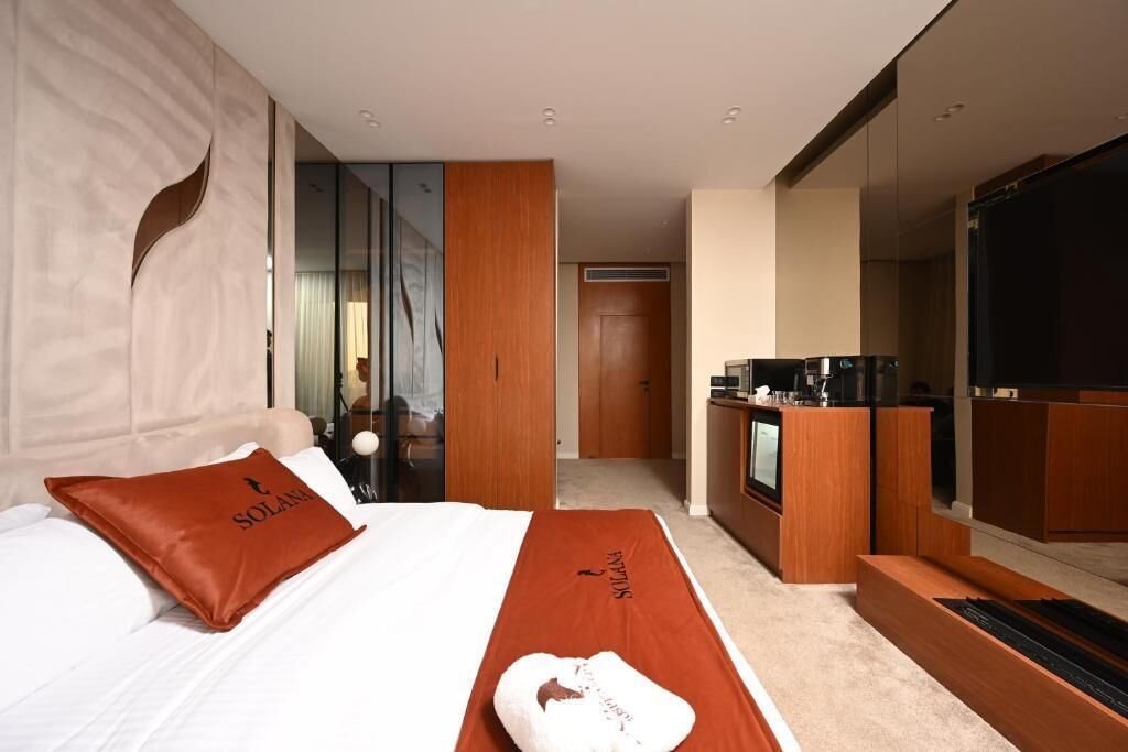 Une chambre d’hôtel avec un lit, un bureau en bois, une télévision et une salle de bain visible à travers une porte en verre.