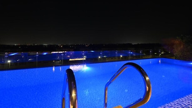 Ein Blick auf ein Schwimmbecken bei Nacht, mit einer Metallleiter und der Skyline der Stadt im Hintergrund.